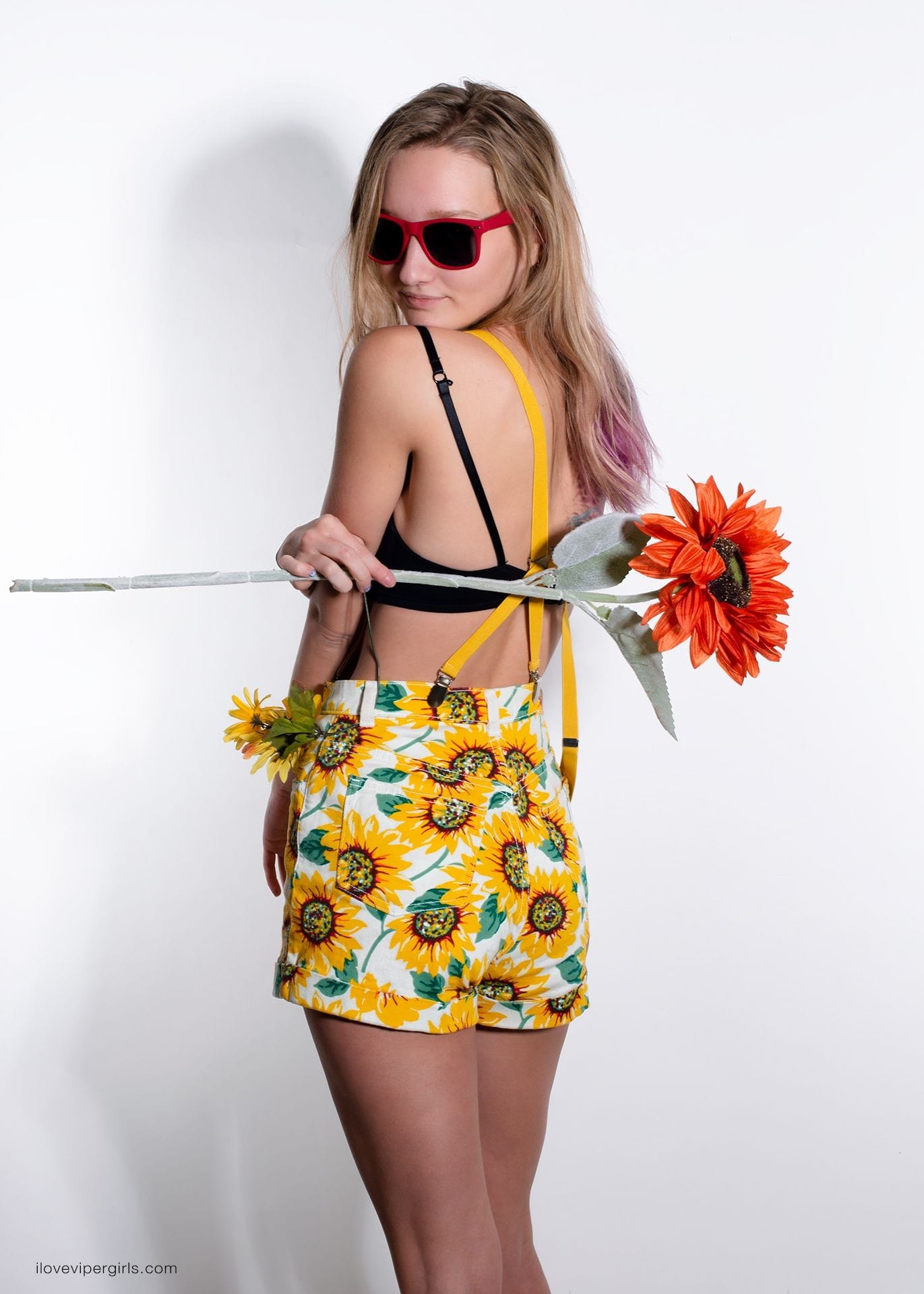 ViperGirls Cheyanne wearing yellow sunflower shorts and holding a red sunflower.
