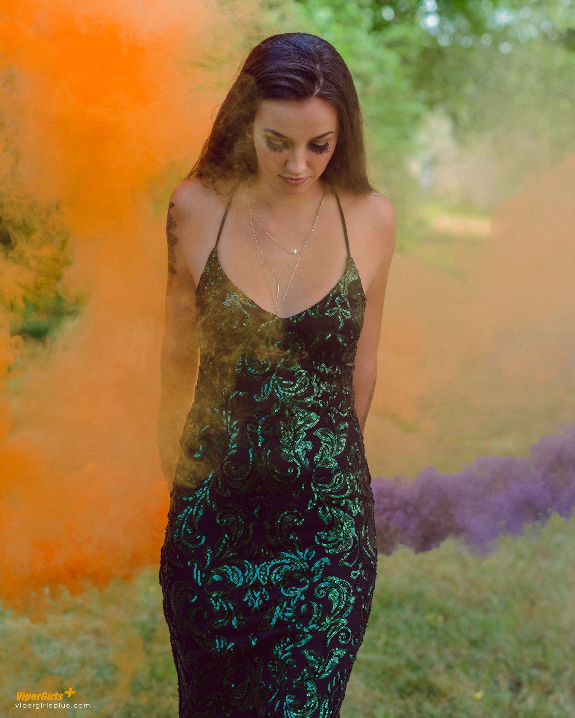 brunesst model wearing a green dress with orange and purple smoke grenades